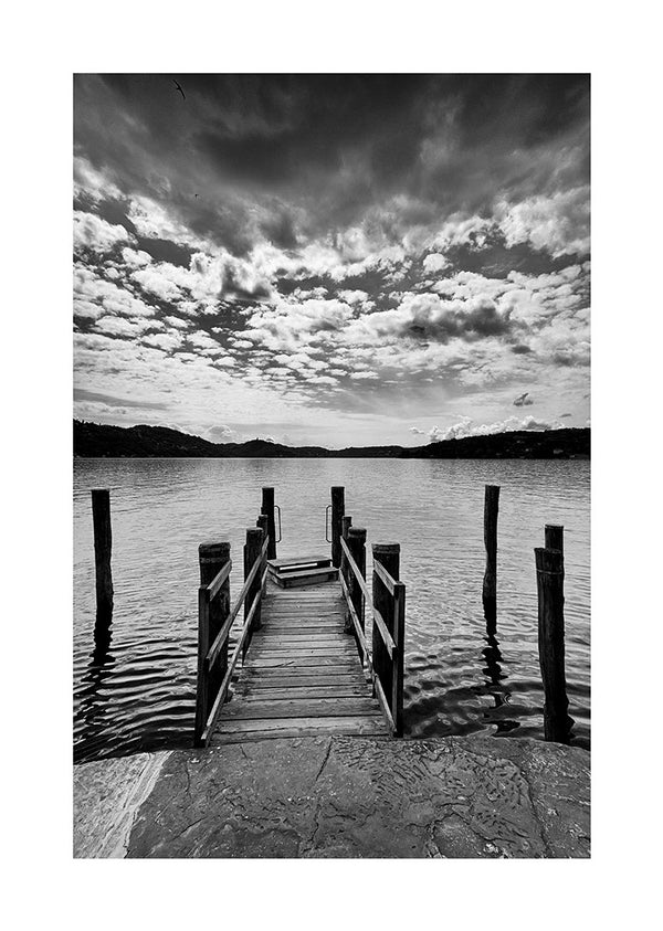 Black and white poster of a wooden bathing jetty extending into a calm lake under a dramatic cloudy sky.