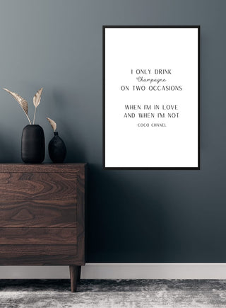 "I drink champagne" poster on a gray wall above a wooden dresser with vases and decorative grasses.