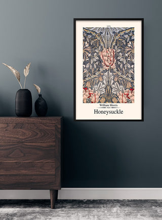 Framed William Morris Honeysuckle poster on a dark wall above a wooden dresser with vase and dried foliage.