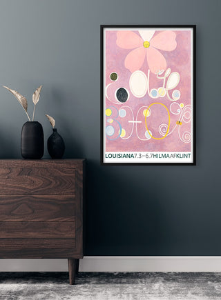 Framed Hilma af Klint Abstrakta Plakat with pink abstract shapes on a dark wall above a wooden dresser.