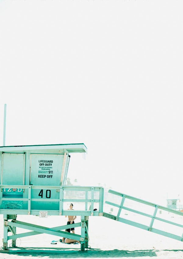 Minimalist photo of a pastel blue lifeguard tower marked "40" on a bright beach, with a lone figure underneath.