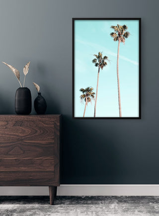 Framed Tall Palms on Beach poster hanging above a wooden dresser in a modern room.