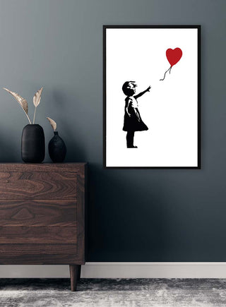 Framed Banksy Girl With Love Balloon artwork on a dark wall above a wooden dresser with decorative vases.