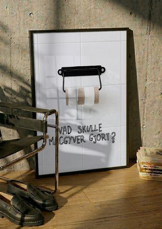 Vad skulle Macgyver gjort? by Grafik bageri in a black frame leaning against a concrete wall by a steel chair