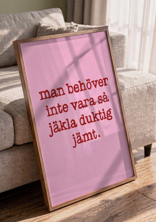 Duktig jämt by Grafik bageri in a walnut frame leaning against a grey sofa