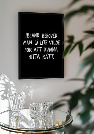 Gå vilse by Grafik bageri in a black frame above a glass table with crystal glassware