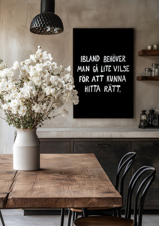 Gå vilse by Grafik bageri in a black frame above a rustic table with white flowers