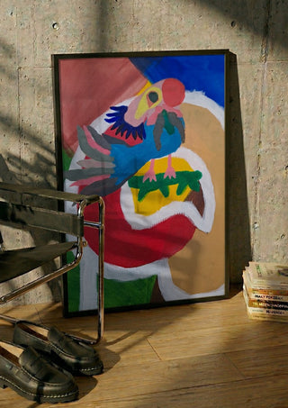 Befriad fågel by Hampus Nerén in a black frame leaning against a concrete wall by a steel chair