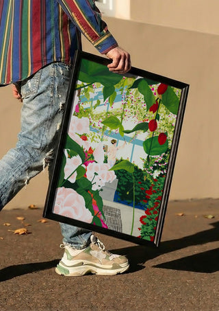 Artist paints in naked workshop by Jaron Su carried in a black frame along a sunny street