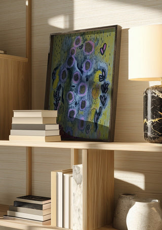 Summer rain by Alice Ruja in a dark frame on a wooden shelf beside books and a lamp