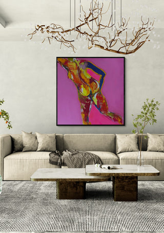 Pink Nude by René J in a black frame above a beige sofa under a branch chandelier