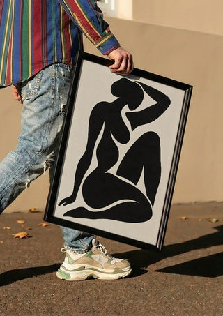 Black Nude Silhouette – Minimalist Abstract Figure Wall Art by TimlessArtworks carried in a black frame along a sunny street