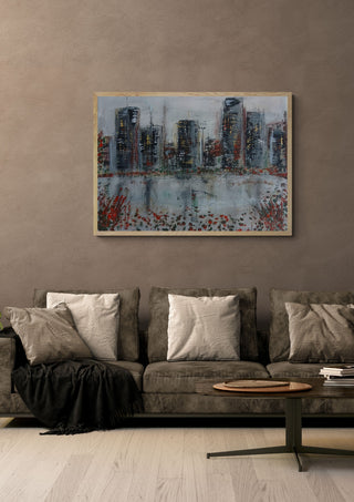 City Across the Water by luco art in a light wood frame above a grey sofa with cushions