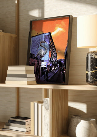 Brick Lane Pelican by Pelecan Schneider in a dark frame on a wooden shelf beside books and a lamp