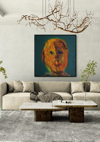 Head in Orange by René J in a black frame above a beige sofa under a branch chandelier