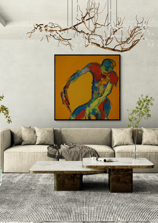 Bending Figure by René J in a black frame above a beige sofa under a branch chandelier