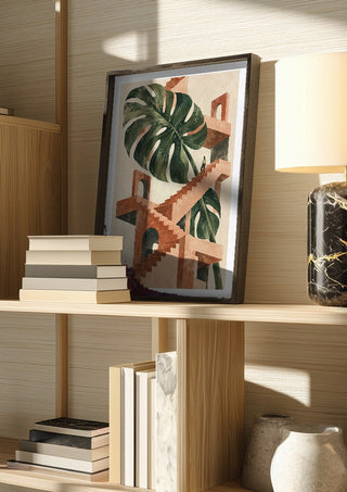 The Green Staircase by Matthews Gallerie in a dark frame on a wooden shelf beside books and a lamp