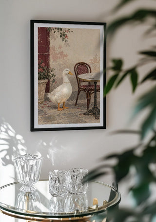 The Duck Wore Pearls by Matthews Gallerie in a black frame above a glass table with crystal glassware