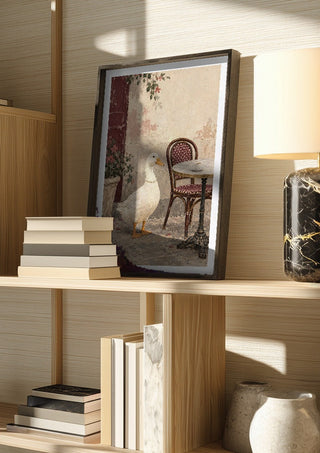 The Duck Wore Pearls by Matthews Gallerie in a dark frame on a wooden shelf beside books and a lamp