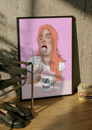 Girl Dinner by Lisen Vennesland in a black frame leaning against a concrete wall by a steel chair