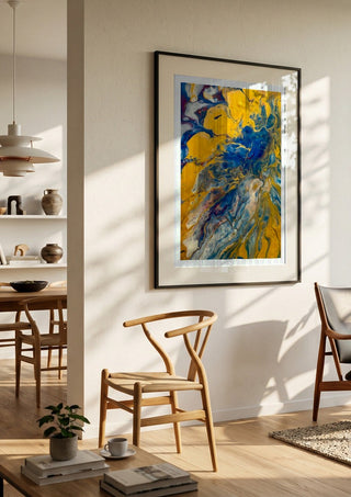 Gold and Indigo by Da Winters in a black frame in a bright dining room with wooden chairs