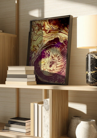 Plum Bloom by Da Winters in a dark frame on a wooden shelf beside books and a lamp