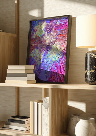 Petal Ridge by Da Winters in a dark frame on a wooden shelf beside books and a lamp