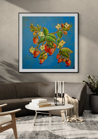 Strawberries on Blue by Svetla Stoyanova Bassi in a black frame above a grey sofa with a round coffee table and candlesticks