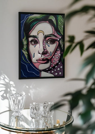 Audrey Hepburn by Okiana in a black frame above a glass table with crystal glassware