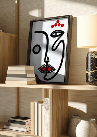 Face by RA in a dark frame on a wooden shelf beside books and a lamp