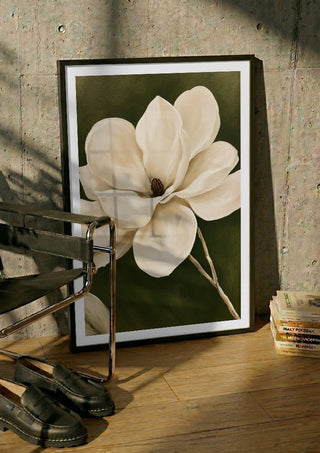 White Magnolia by Martina Karlsson in a black frame leaning against a concrete wall by a steel chair