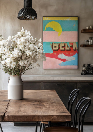 BEL-M by Kareem Rizk in a black frame above a rustic table with white flowers