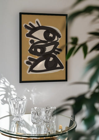 Abstract line art eyes 10 by ThingDesign in a black frame above a glass table with crystal glassware