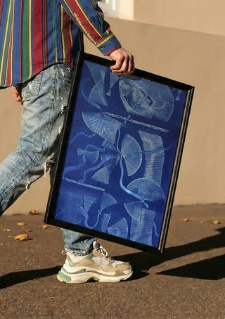 Curved lines / blue field by Linor Citaku carried in a black frame along a sunny street