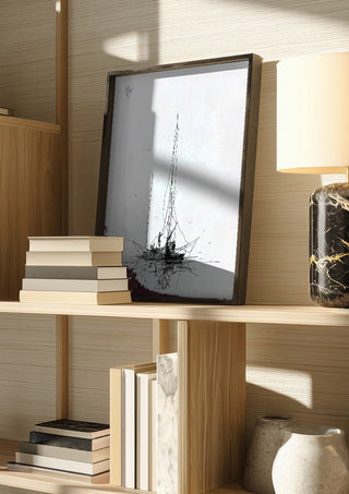 Two Masts by Justyna Kopania in a dark frame on a wooden shelf beside books and a lamp