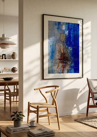 Ship in Blue by Justyna Kopania in a black frame in a bright dining room with wooden chairs