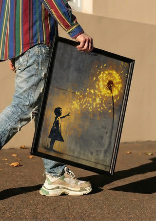 Golden Dandeloin x Banksy by Decker Studios carried in a black frame along a sunny street