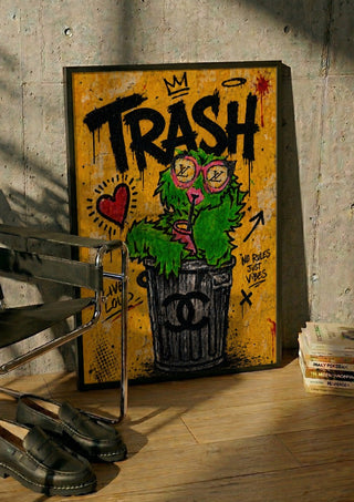 Trash x Grafitti by Decker Studios in a black frame leaning against a concrete wall by a steel chair