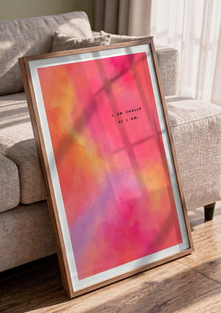 I Am Enough by Decker Studios in a walnut frame leaning against a grey sofa