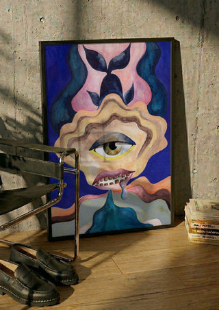 The Weeping Eye by Shimmering Ugly in a black frame leaning against a concrete wall by a steel chair