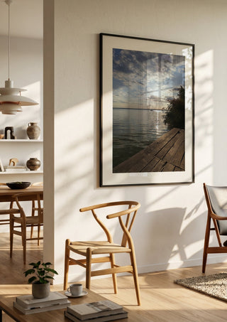 Sunset at the Lakeside Dock by Bora Kőhalmi in a black frame in a bright dining room with wooden chairs