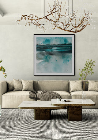 Reflections by Tania Zubareva in a black frame above a beige sofa under a branch chandelier