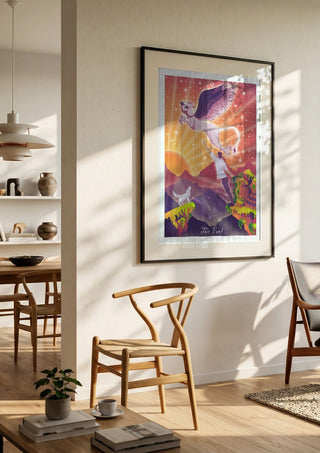 The Fool by Sciurus tarotus in a black frame in a bright dining room with wooden chairs