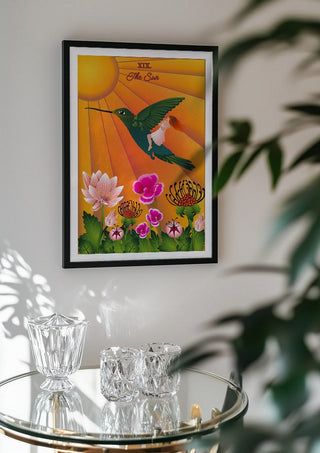 The Sun by Sciurus tarotus in a black frame above a glass table with crystal glassware