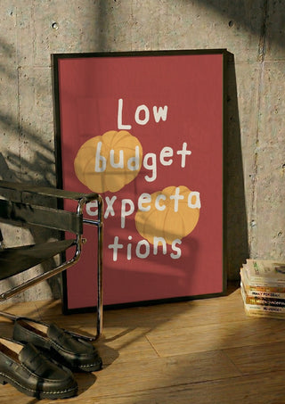 Low Budget Expectations by Jakob Falkenberg in a black frame leaning against a concrete wall by a steel chair