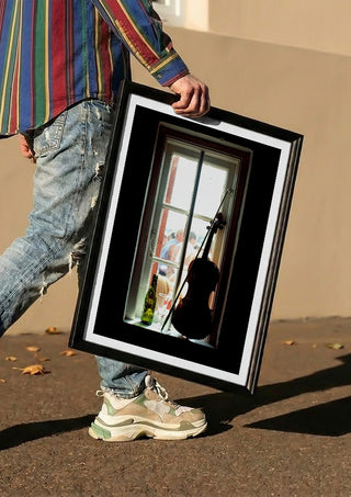 A Nice Day by Bent Hardervig carried in a black frame along a sunny street