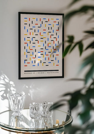 Bauhaus Dashes by Neil Stevens in a black frame above a glass table with crystal glassware
