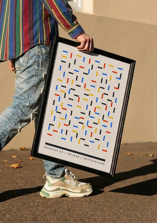 Bauhaus Dashes by Neil Stevens carried in a black frame along a sunny street