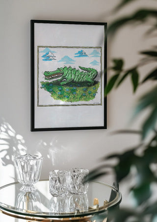 The Crocodile and the Book by Waldemar Mandzel in a black frame above a glass table with crystal glassware