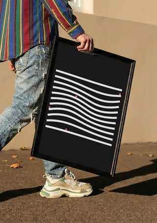 Marbels by Aleksi Allan carried in a black frame along a sunny street